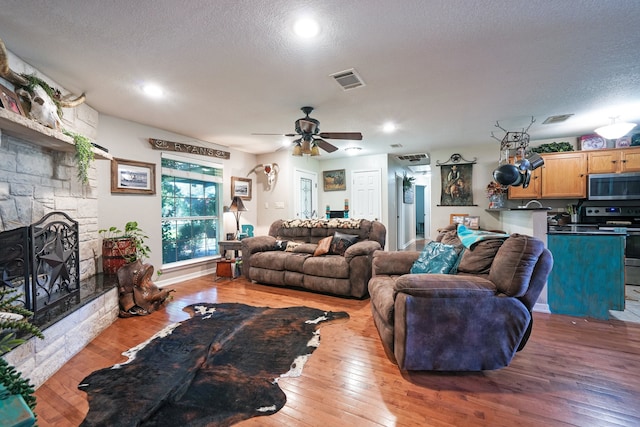 living room with ceiling fan, a fireplace, light hardwood / wood-style floors, and a textured ceiling