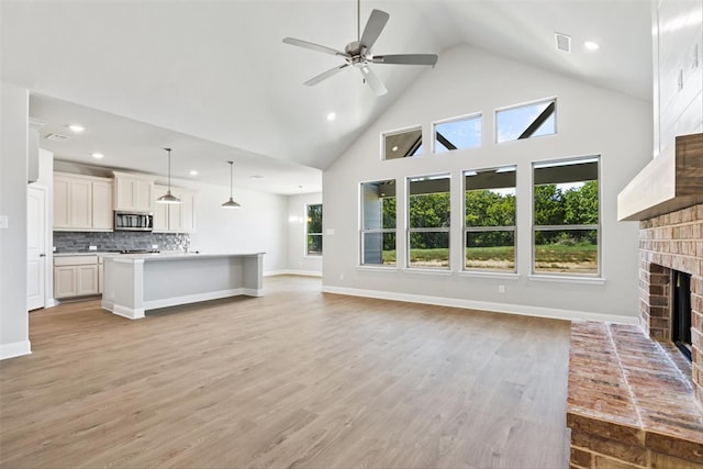 unfurnished living room featuring a fireplace, light hardwood / wood-style floors, high vaulted ceiling, and ceiling fan