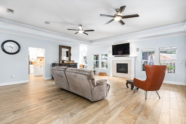 living room with a tile fireplace, light wood-type flooring, ceiling fan, and a raised ceiling