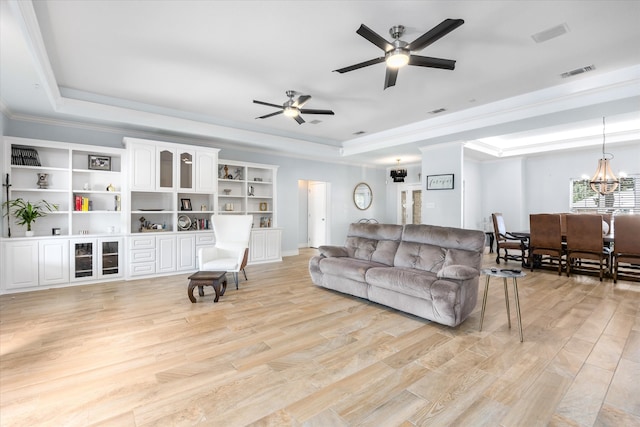 living room with ceiling fan with notable chandelier, ornamental molding, light hardwood / wood-style floors, and a tray ceiling