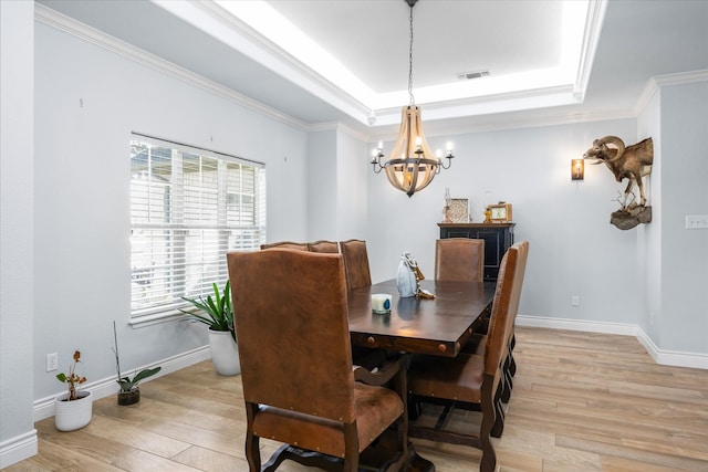 dining area with a notable chandelier, light wood-type flooring, a raised ceiling, and ornamental molding