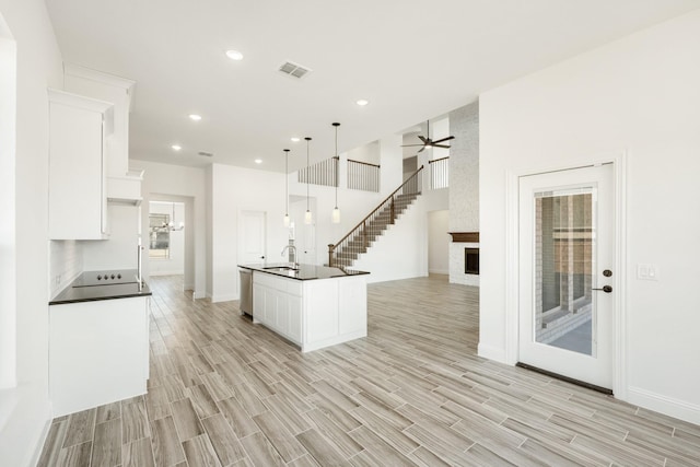 kitchen featuring pendant lighting, a fireplace, dishwasher, white cabinets, and a kitchen island with sink