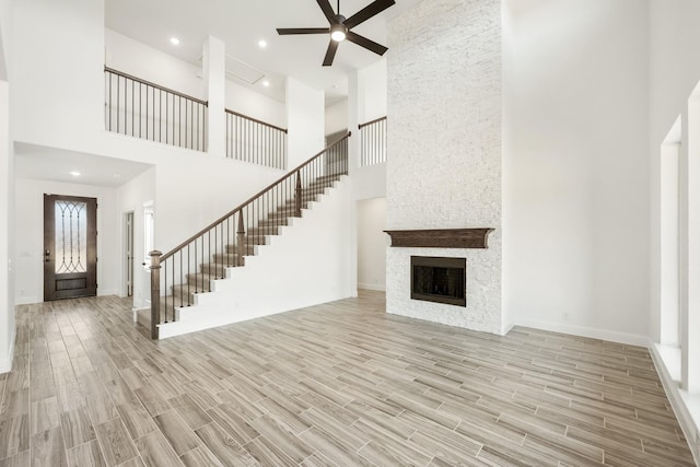 unfurnished living room with ceiling fan, a towering ceiling, and a fireplace