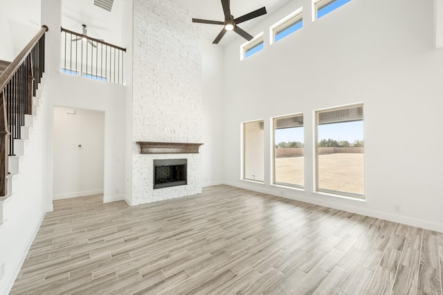 unfurnished living room with ceiling fan, a towering ceiling, and a stone fireplace