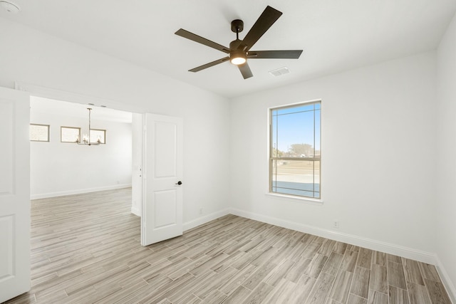 spare room featuring ceiling fan with notable chandelier and light wood-type flooring