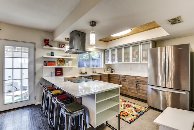 kitchen with stainless steel refrigerator, island range hood, kitchen peninsula, and a breakfast bar