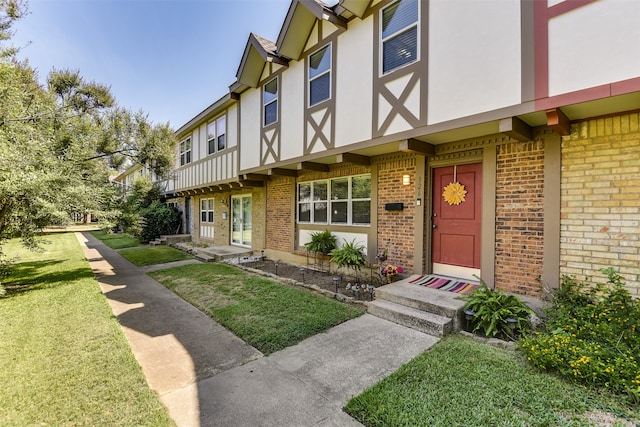 view of exterior entry featuring a yard, brick siding, and stucco siding