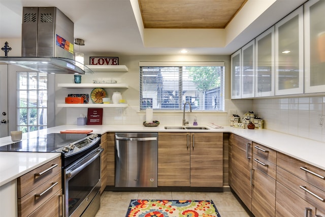 kitchen with light tile patterned flooring, island range hood, stainless steel appliances, a sink, and backsplash