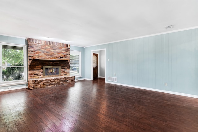 unfurnished living room featuring a brick fireplace, wooden walls, crown molding, and dark hardwood / wood-style flooring