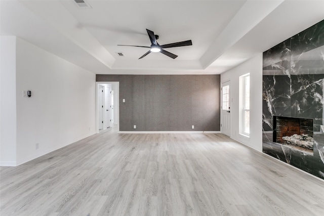 unfurnished living room featuring light wood-type flooring, ceiling fan, a high end fireplace, and a raised ceiling