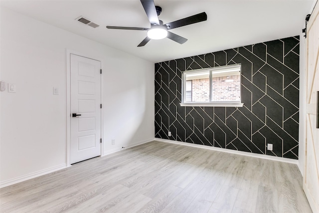 unfurnished room with ceiling fan, light hardwood / wood-style flooring, and a barn door