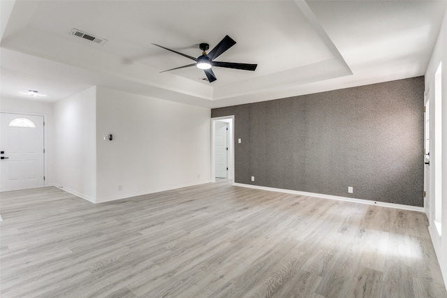 spare room featuring a raised ceiling, ceiling fan, and light hardwood / wood-style floors