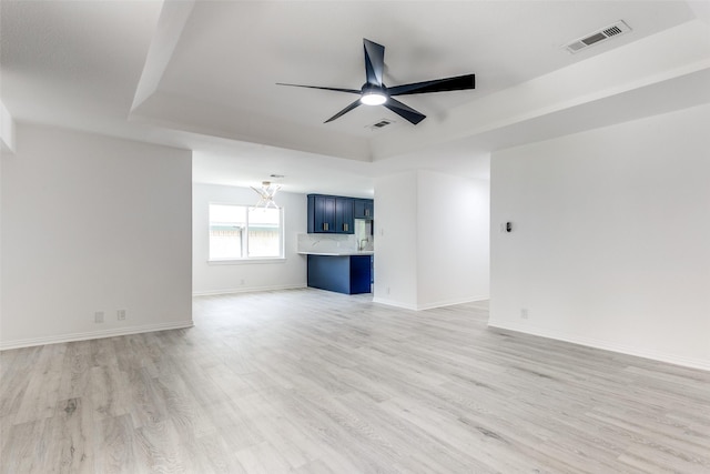 unfurnished living room featuring a raised ceiling, ceiling fan with notable chandelier, and light hardwood / wood-style floors