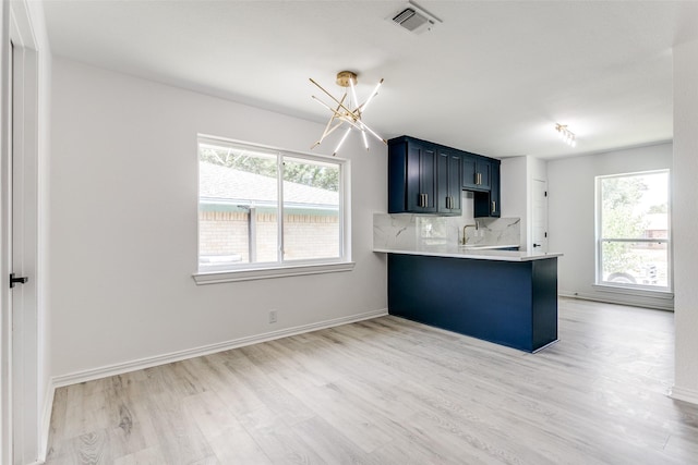 kitchen featuring a notable chandelier, light hardwood / wood-style floors, kitchen peninsula, decorative backsplash, and a kitchen breakfast bar