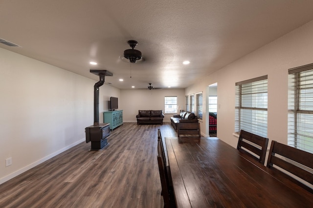 cinema room featuring a textured ceiling, dark hardwood / wood-style floors, ceiling fan, and a wood stove