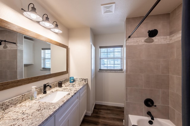 bathroom with a healthy amount of sunlight, tiled shower / bath combo, hardwood / wood-style floors, and vanity