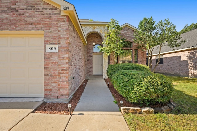 doorway to property with a garage and brick siding