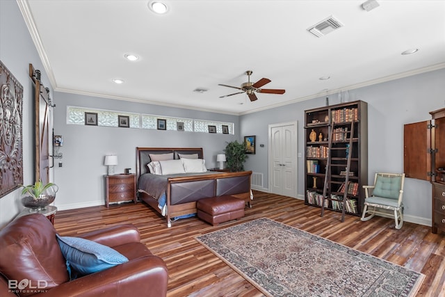 bedroom featuring ceiling fan, a barn door, hardwood / wood-style flooring, and crown molding