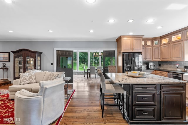 kitchen with tasteful backsplash, light stone countertops, black refrigerator with ice dispenser, a center island, and dark hardwood / wood-style floors