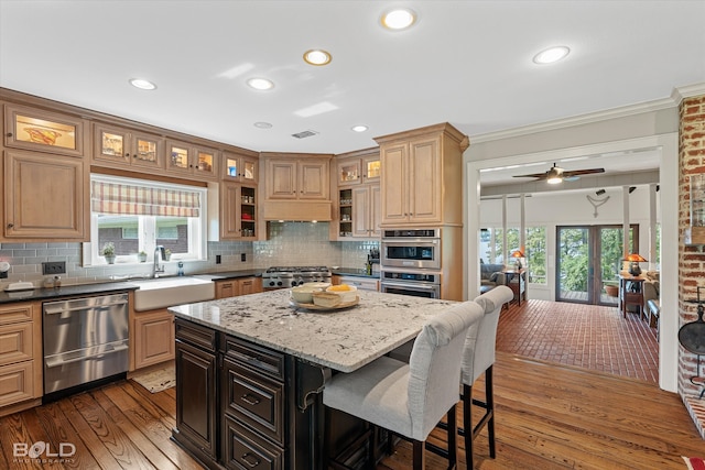 kitchen featuring appliances with stainless steel finishes, backsplash, ceiling fan, sink, and a kitchen island