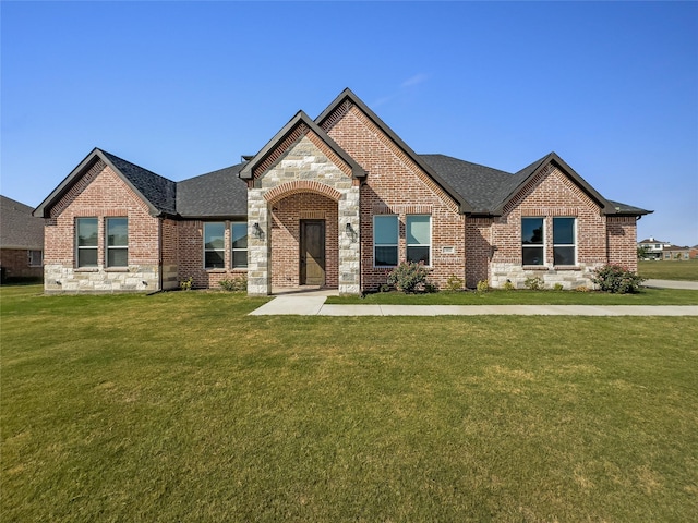 view of front of property featuring stone siding, brick siding, roof with shingles, and a front yard