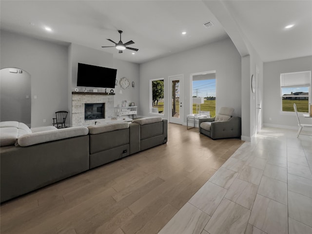 living room with arched walkways, a ceiling fan, a glass covered fireplace, light wood-style flooring, and recessed lighting