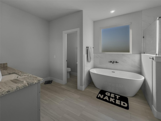 full bath featuring tile walls, a freestanding tub, vanity, and toilet