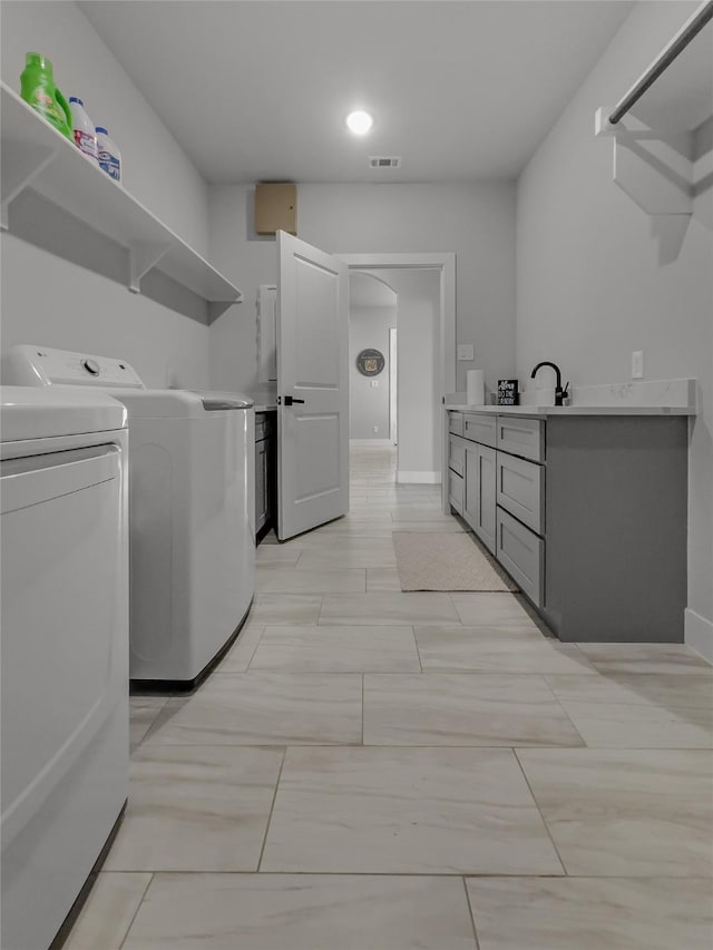 laundry area featuring laundry area, visible vents, arched walkways, washing machine and dryer, and a sink