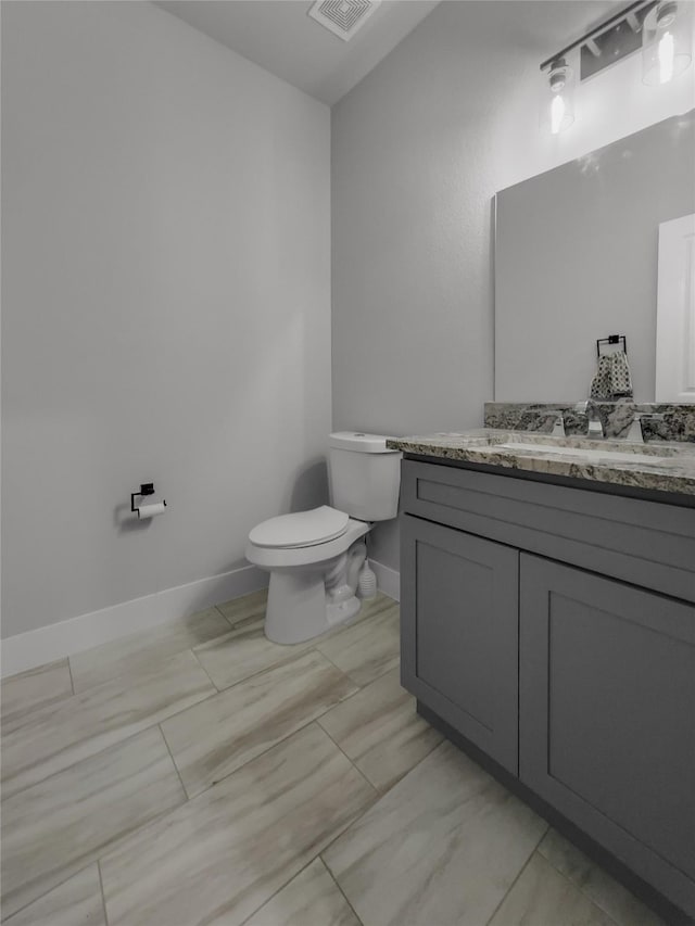 half bath featuring baseboards, visible vents, vanity, and toilet