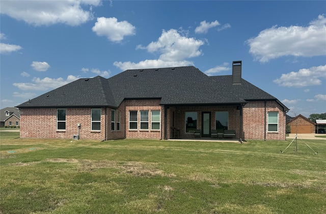 rear view of house featuring a shingled roof, a lawn, a chimney, a patio area, and brick siding