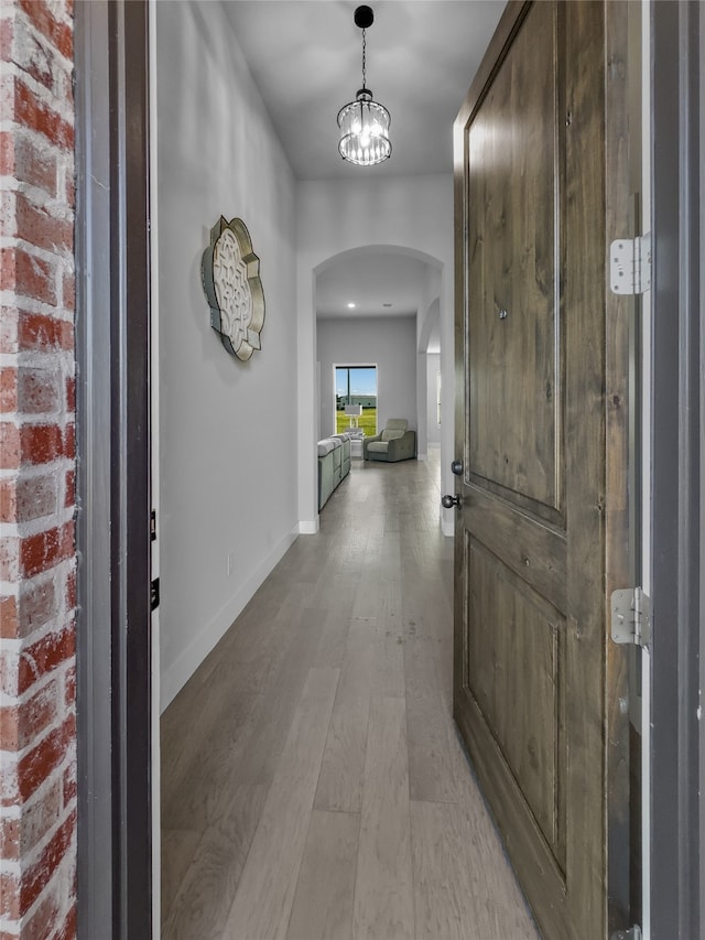 entryway featuring light wood-type flooring, an inviting chandelier, and brick wall