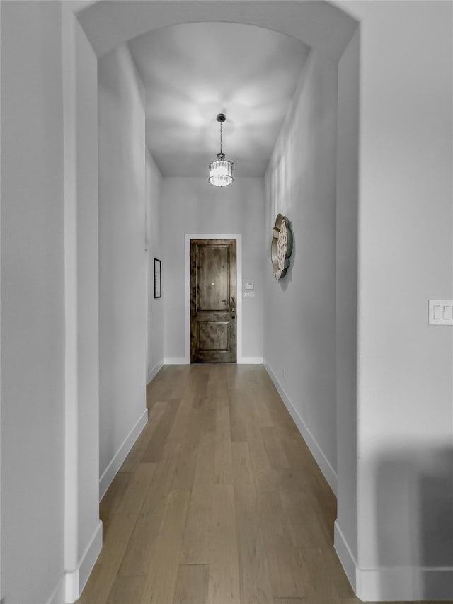 hallway featuring a chandelier, arched walkways, baseboards, and light wood finished floors