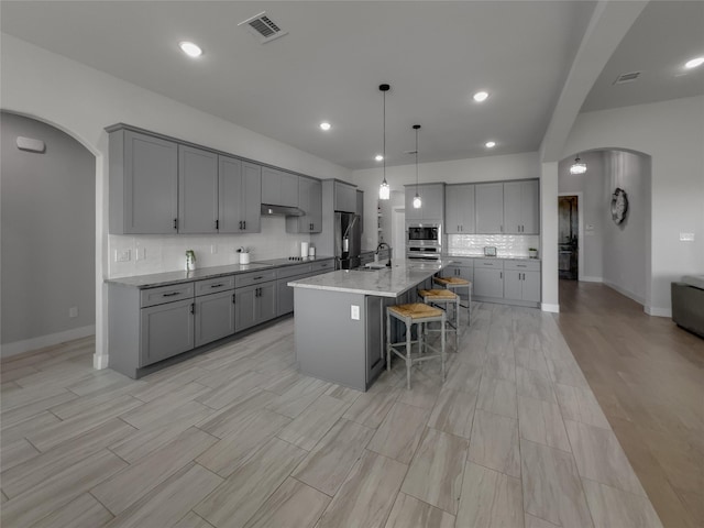 kitchen featuring an island with sink, gray cabinets, arched walkways, and stainless steel appliances