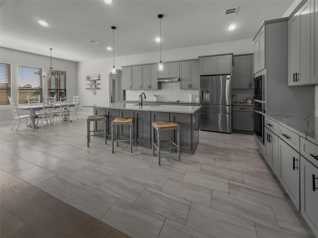 kitchen with visible vents, appliances with stainless steel finishes, hanging light fixtures, light stone countertops, and gray cabinetry