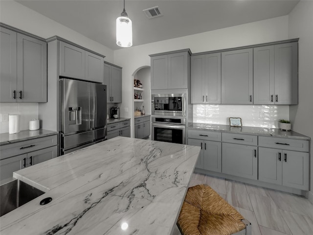 kitchen featuring stainless steel appliances, light stone counters, gray cabinets, and pendant lighting