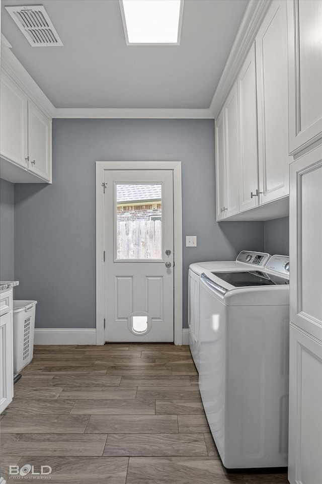 laundry room with cabinets, light wood-type flooring, crown molding, and washer and clothes dryer