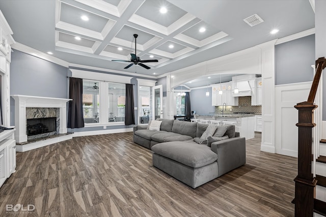 living room featuring crown molding, coffered ceiling, a premium fireplace, ceiling fan, and dark hardwood / wood-style floors