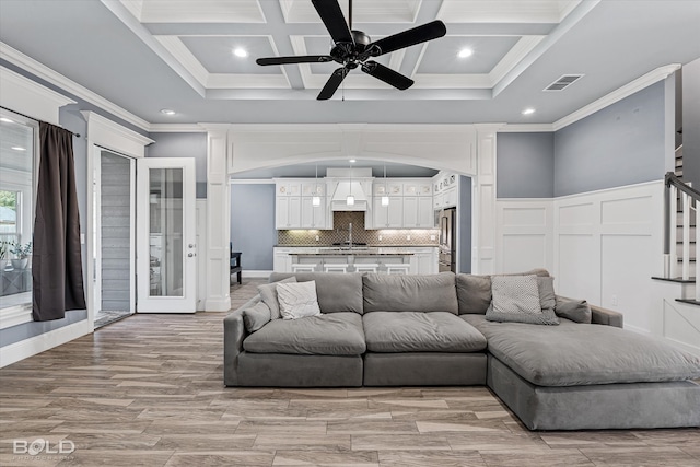 living room with coffered ceiling, ornamental molding, beamed ceiling, and ceiling fan