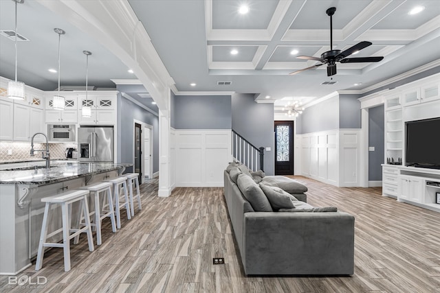 living room with ceiling fan with notable chandelier, crown molding, light hardwood / wood-style floors, beam ceiling, and coffered ceiling