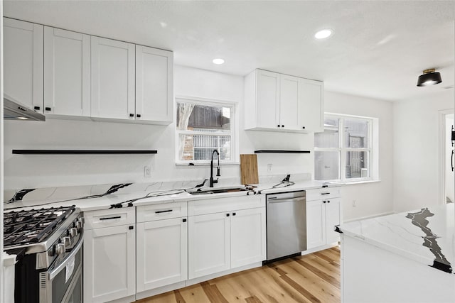 kitchen featuring white cabinetry, sink, range hood, light hardwood / wood-style floors, and appliances with stainless steel finishes