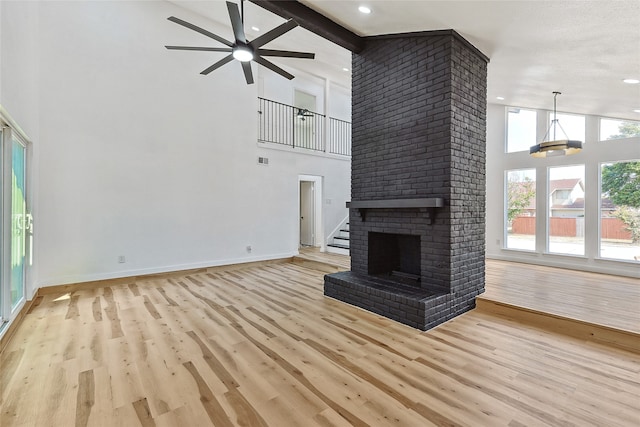 unfurnished living room with beam ceiling, ceiling fan, a brick fireplace, high vaulted ceiling, and light wood-type flooring