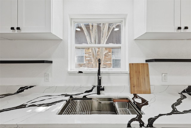 room details with light stone counters, sink, and white cabinets