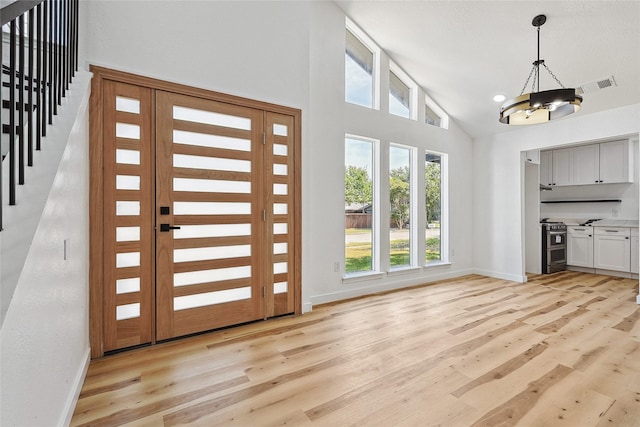 entryway featuring a chandelier, high vaulted ceiling, light wood-style flooring, visible vents, and baseboards