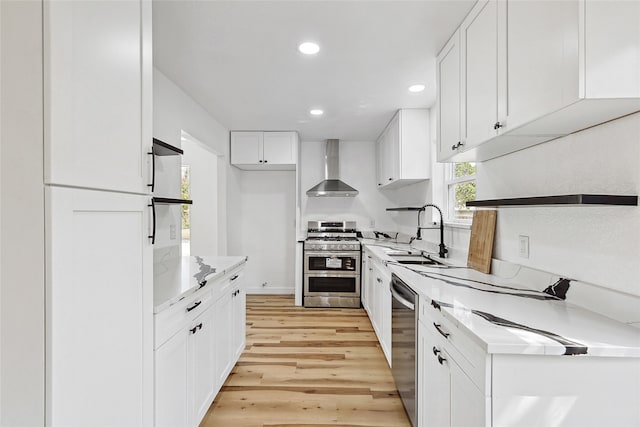 kitchen featuring white cabinetry, sink, wall chimney range hood, appliances with stainless steel finishes, and light wood-type flooring