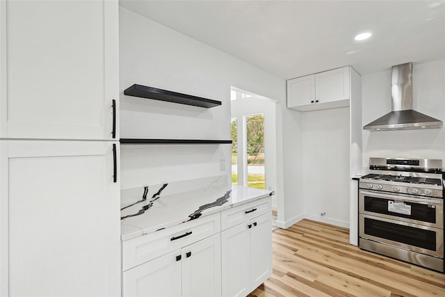 kitchen featuring light stone counters, wall chimney range hood, range with two ovens, white cabinets, and light hardwood / wood-style floors