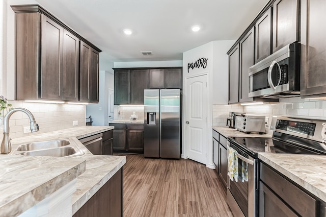 kitchen with appliances with stainless steel finishes, sink, dark brown cabinetry, tasteful backsplash, and dark hardwood / wood-style flooring