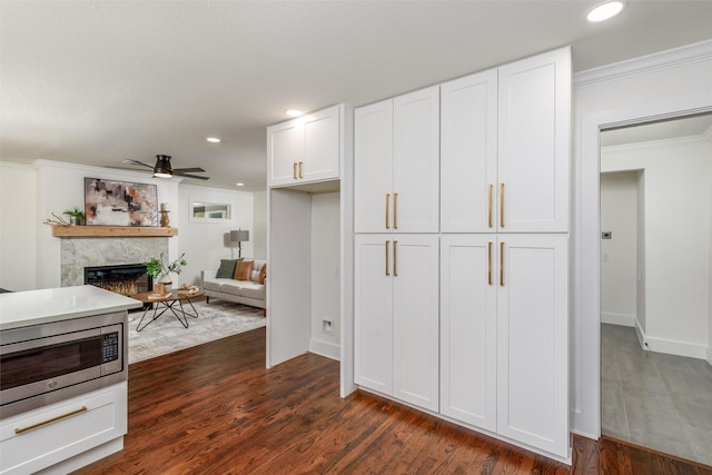 kitchen with stainless steel microwave, white cabinets, dark hardwood / wood-style flooring, ceiling fan, and crown molding