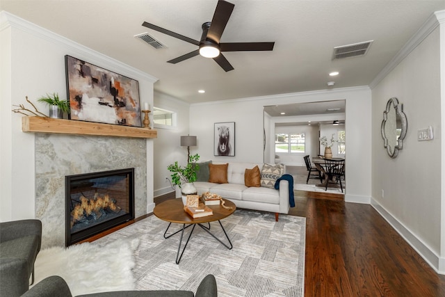 living room featuring a fireplace, crown molding, dark wood-type flooring, and ceiling fan