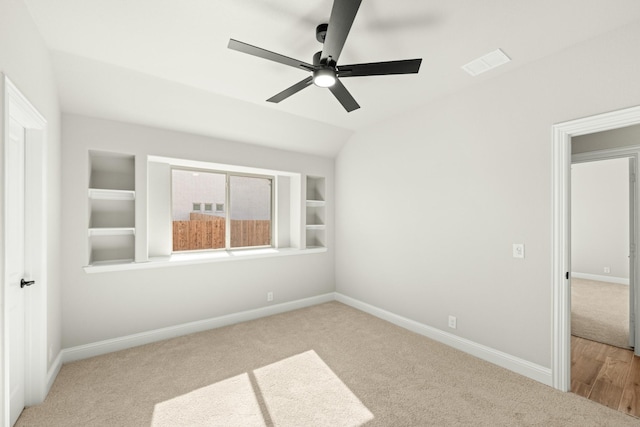 interior space with vaulted ceiling, light colored carpet, ceiling fan, and built in shelves