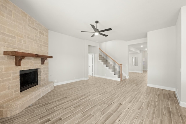 unfurnished living room featuring ceiling fan, a stone fireplace, and light wood-type flooring